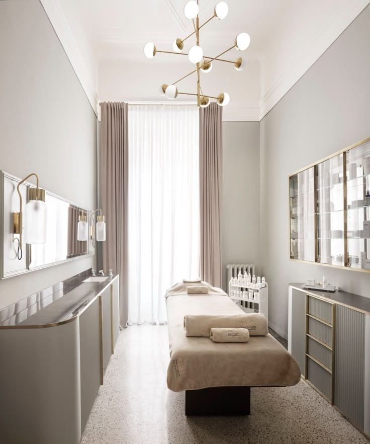 Sala trattamenti dello studio Verdiva, con lettino coperto da tessuto color sabbia, lampadario in ottone e mobili chiari